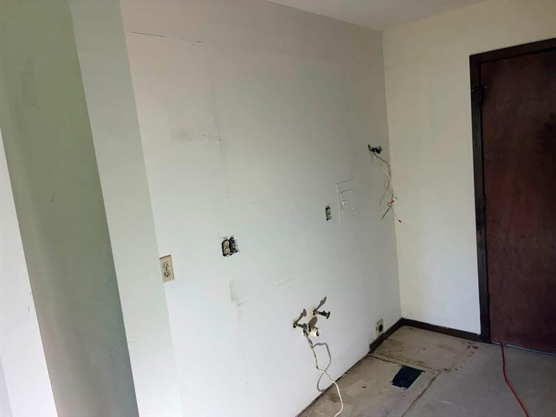 Bare kitchen wall with plumbing stub-outs and exposed electrical, floor torn up.