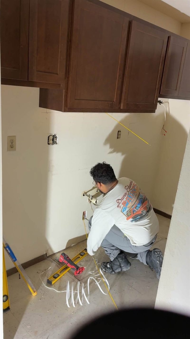 A worker measuring and marking the wall with the upper cabinets already hung.