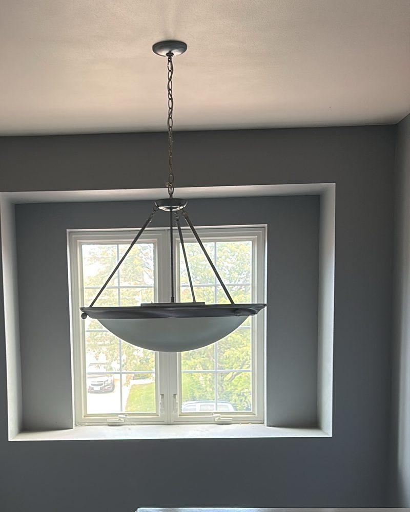 A two-story foyer with an old frosted bowl pendant on a chain hanging in front of the window above the front door.
