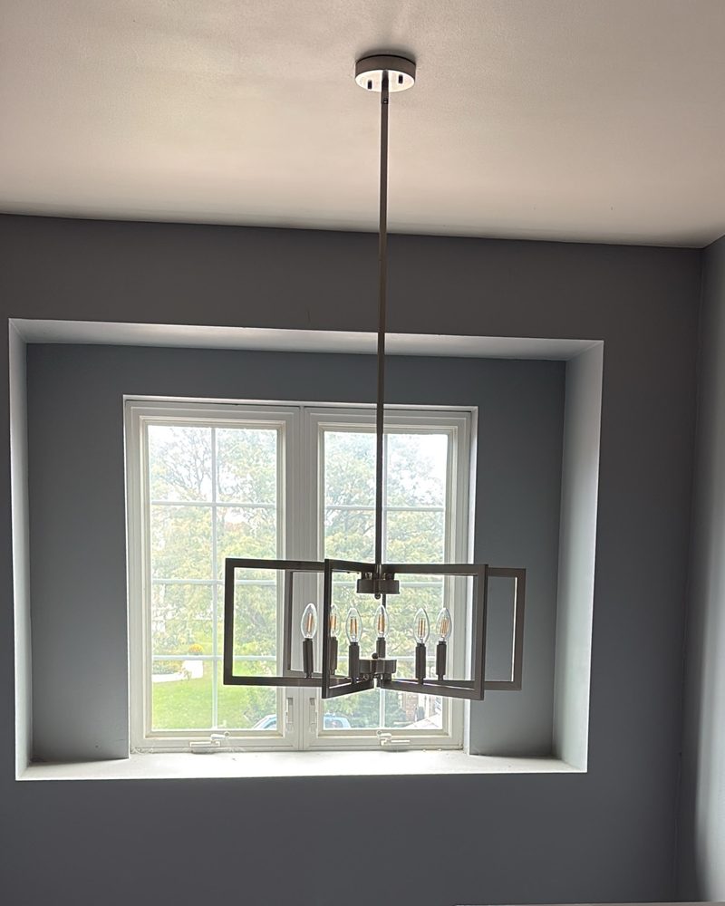 The same two-story foyer with a new six-light geometric fixture hanging in front of the window.