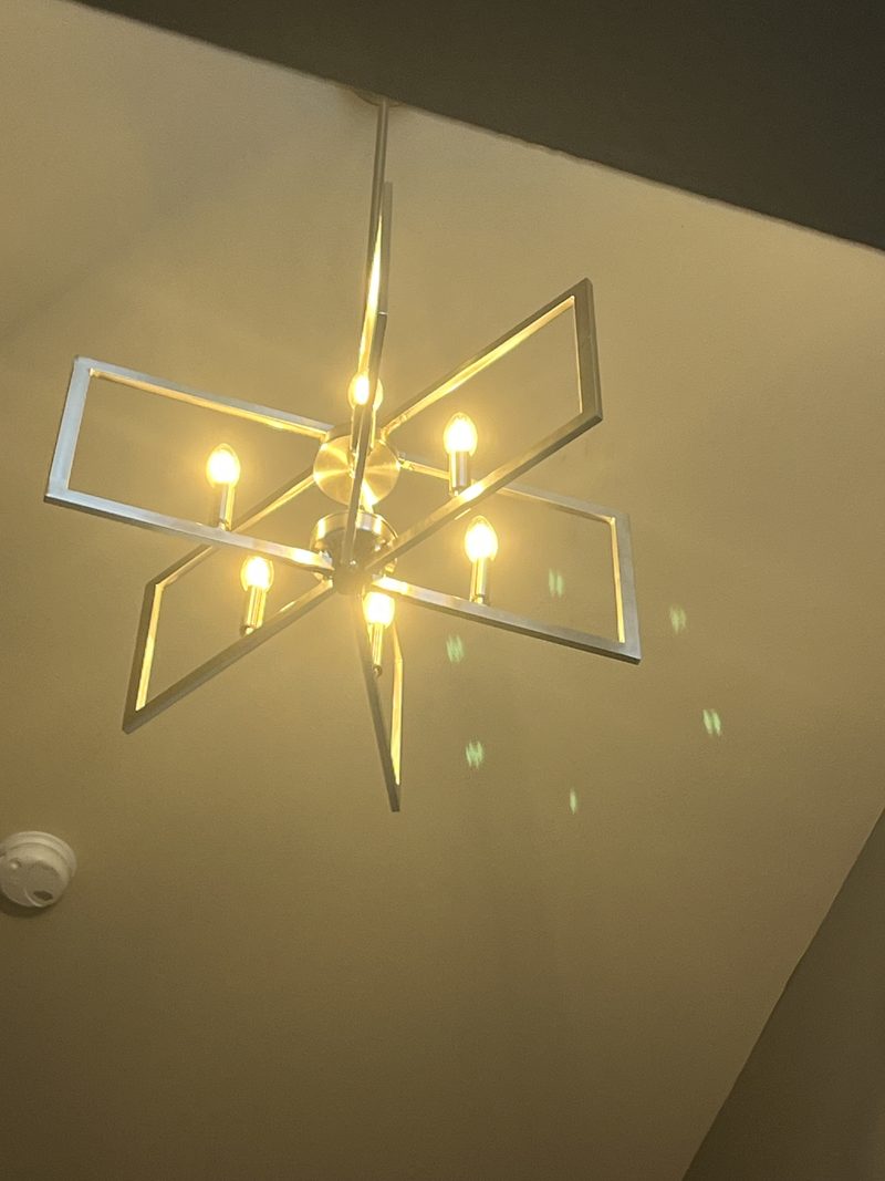 The new fixture seen from below with all six candle bulbs lit, casting light patterns on the ceiling.