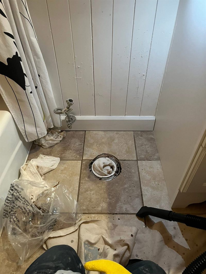 Bathroom floor with the old toilet removed and the flange exposed, with rags and a shop vacuum nearby.