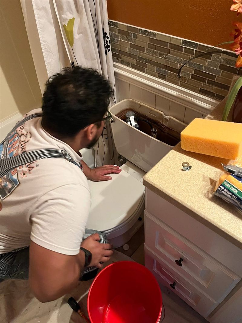 A 10-4 Handyman worker setting the new toilet into place, with the floor protected.