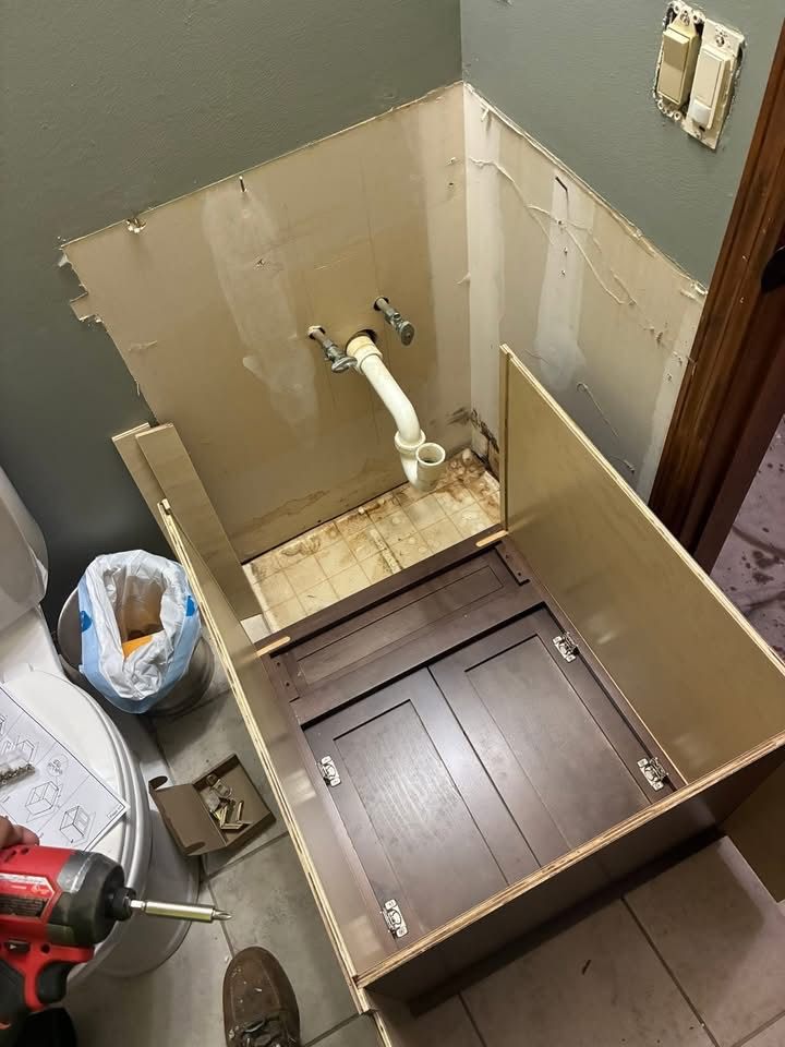 A bathroom vanity cabinet being assembled, with the wall opened up and the plumbing stub visible.