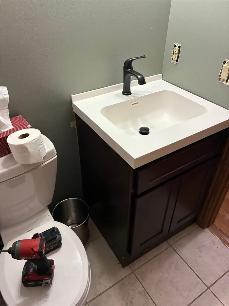 A finished bathroom vanity with a white top, dark cabinet and black faucet.