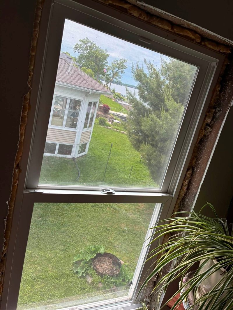 A window with its trim removed, showing the bare rough opening, old caulk and exposed insulation.